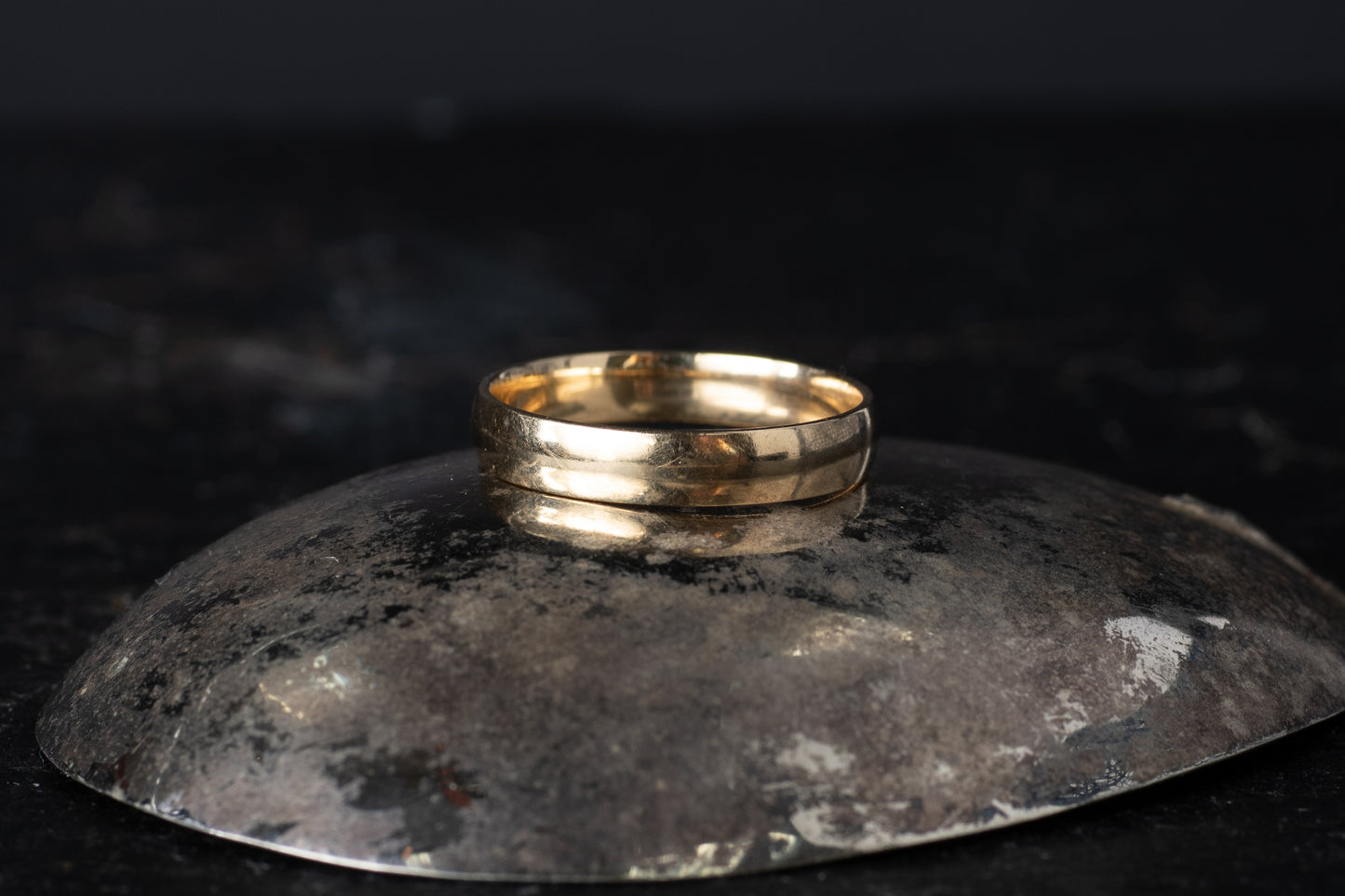 Plain 9ct yellow gold vintage mens wedding band ring resting on a dark reflective surface.