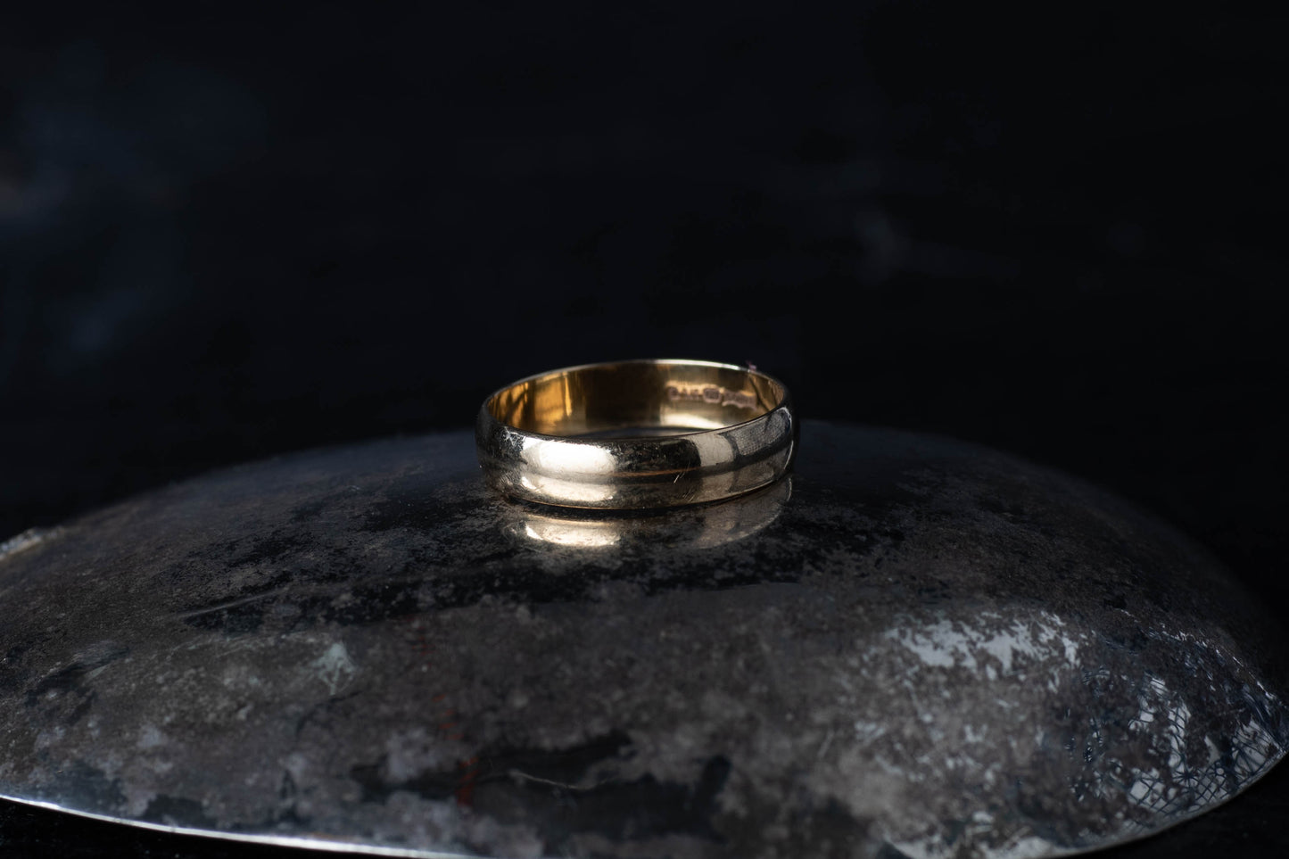9ct yellow gold wedding band ring resting on a dark reflective surface.