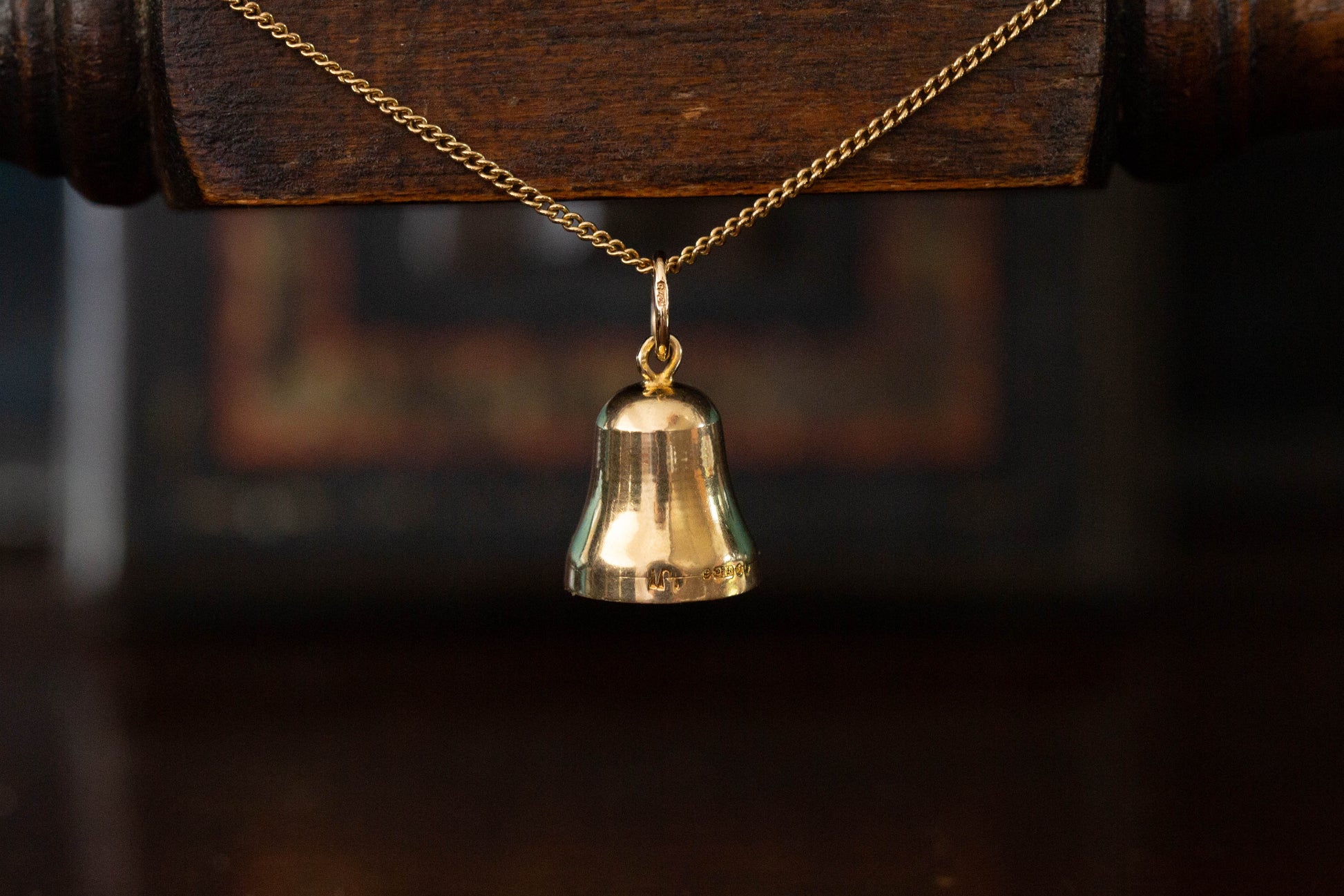 Close up of 9ct yellow gold bell pendant charm hanging against a dark wooden background.
