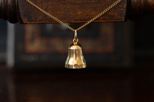 Close up of 9ct yellow gold bell pendant charm hanging against a dark wooden background.