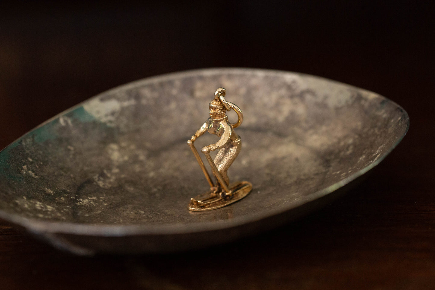 9ct yellow gold skier pendant charm standing on skis on a dark reflective background.