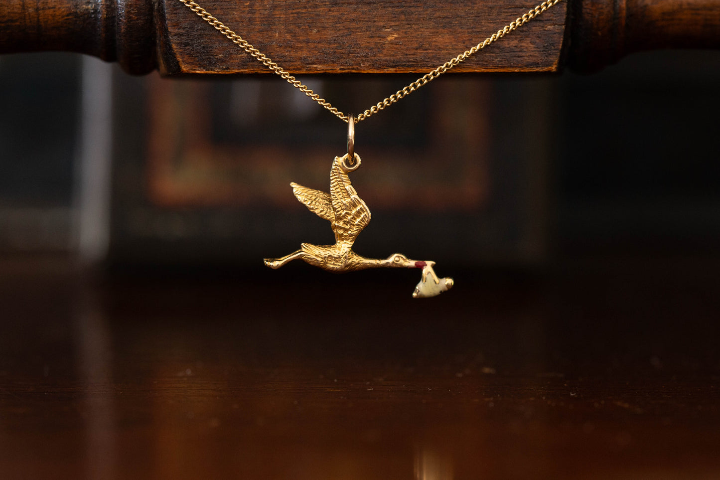 9ct yellow gold stork pendant charm carrying a baby bundle hanging against a dark background.