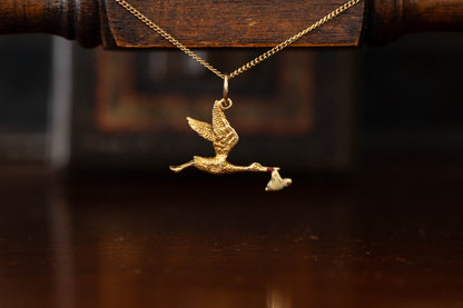 9ct yellow gold stork pendant charm carrying a baby bundle hanging against a dark background.