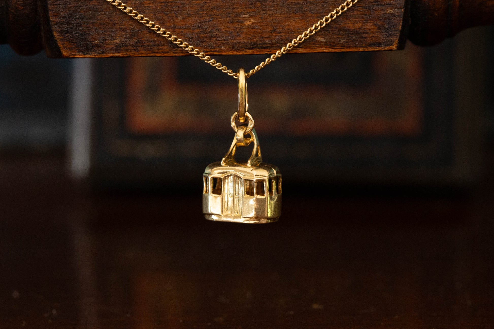 14ct yellow gold gondola cable car pendant charm hanging against a dark wooden background.