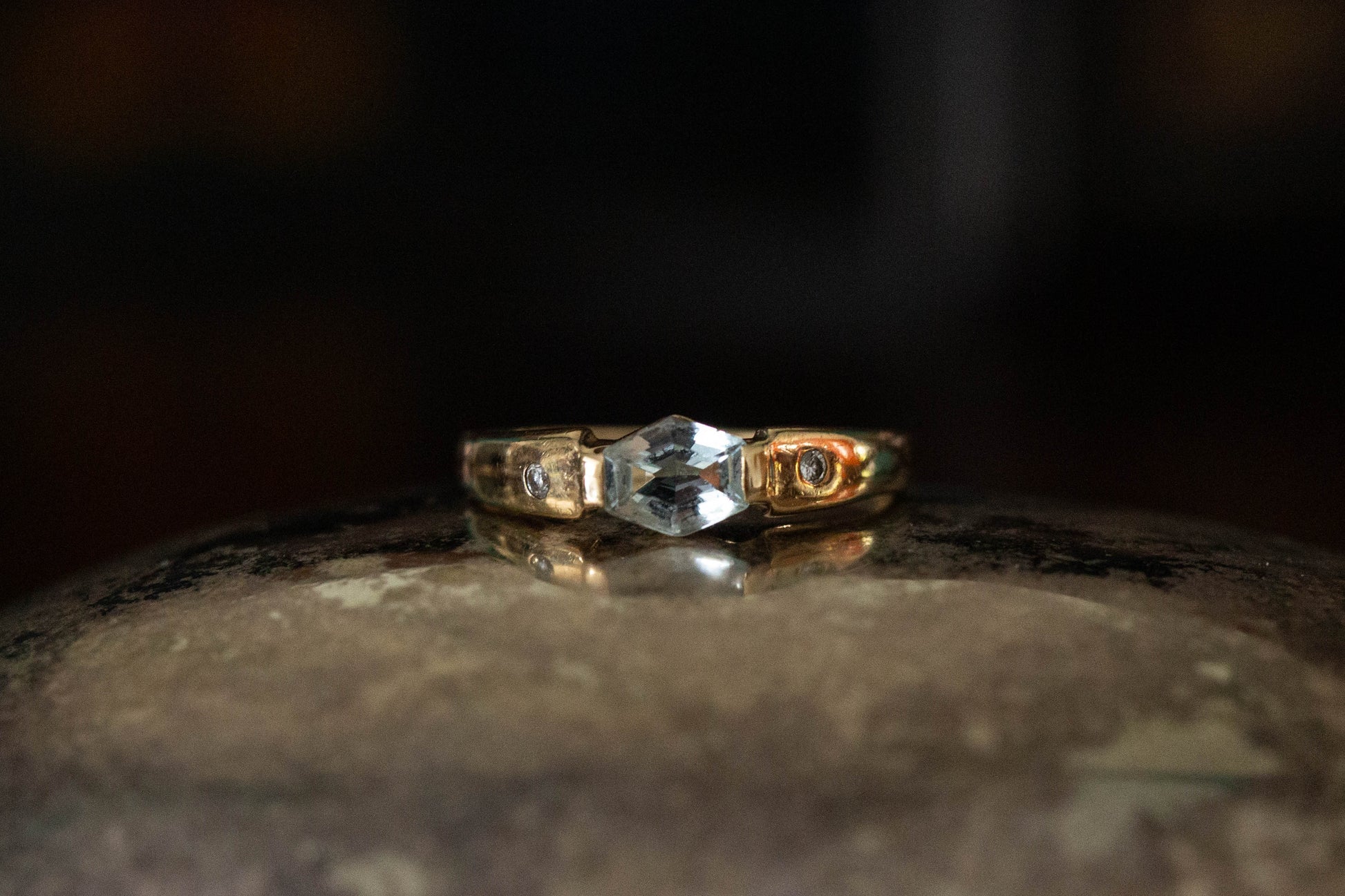 9ct yellow gold ring featuring rub-over set hexagonal aquamarine and diamond accents on a dark reflective surface.
