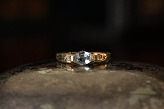 9ct yellow gold ring featuring rub-over set hexagonal aquamarine and diamond accents on a dark reflective surface.