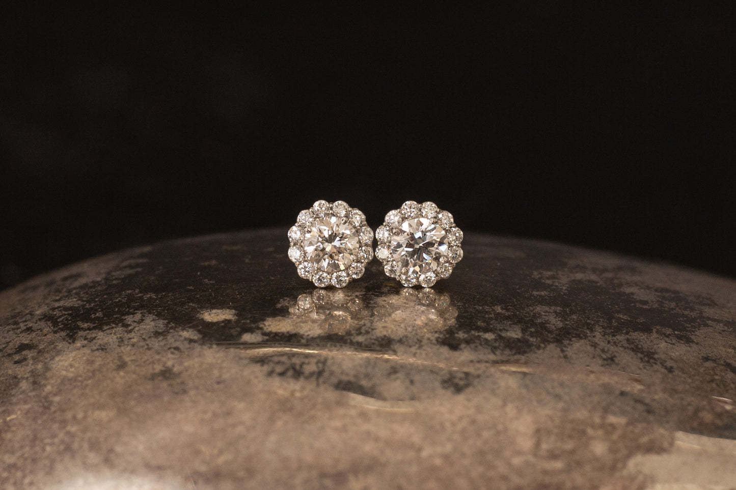 Platinum daisy cluster diamond stud earrings resting on textured metallic surface with black background.