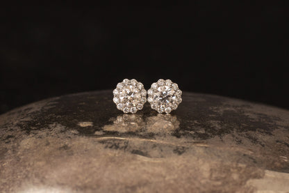 Platinum daisy cluster diamond stud earrings resting on textured metallic surface with black background.