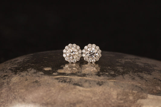 Platinum daisy cluster diamond stud earrings resting on textured metallic surface with black background.