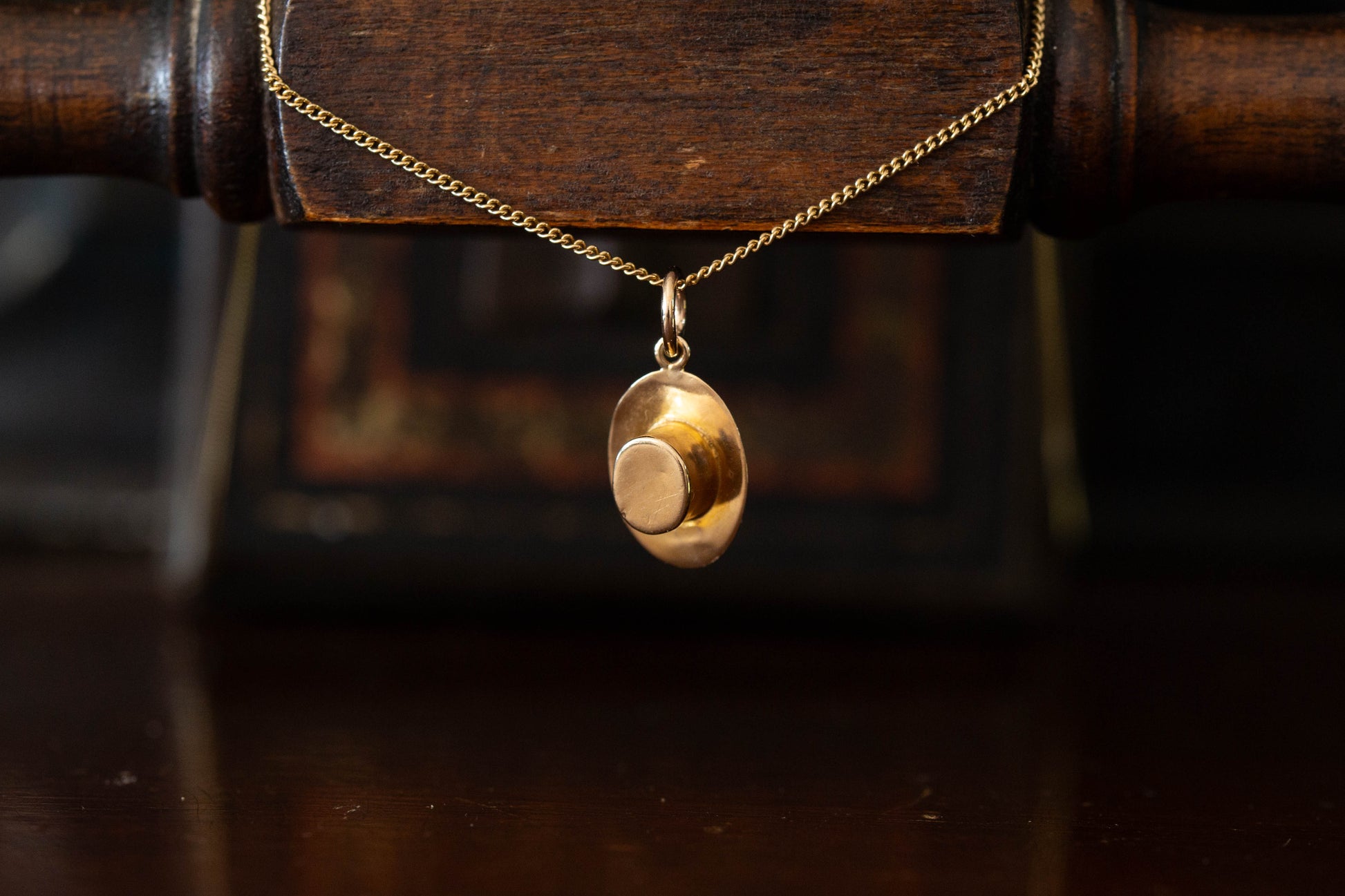 Close up of 9ct yellow gold hat shaped pendant charm hanging against a dark wooden background.