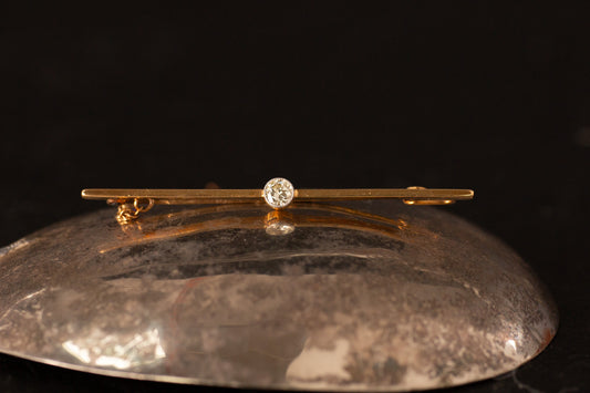 15ct yellow gold bar brooch with platinum set old cut diamond and safety chain on dark reflective surface.