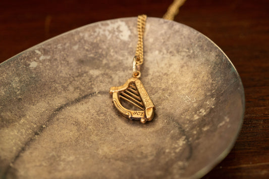 9ct yellow gold harp pendant charm with engraved details lying on a dark metallic dish.
