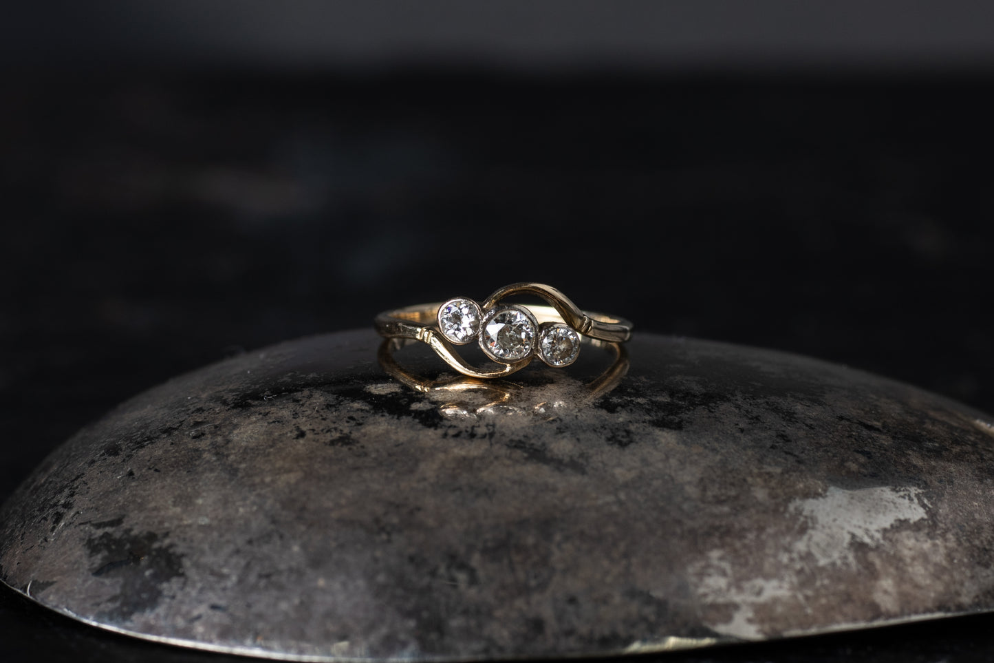 18ct yellow gold antique twist ring featuring three rub-over set diamonds on a dark reflective background.
