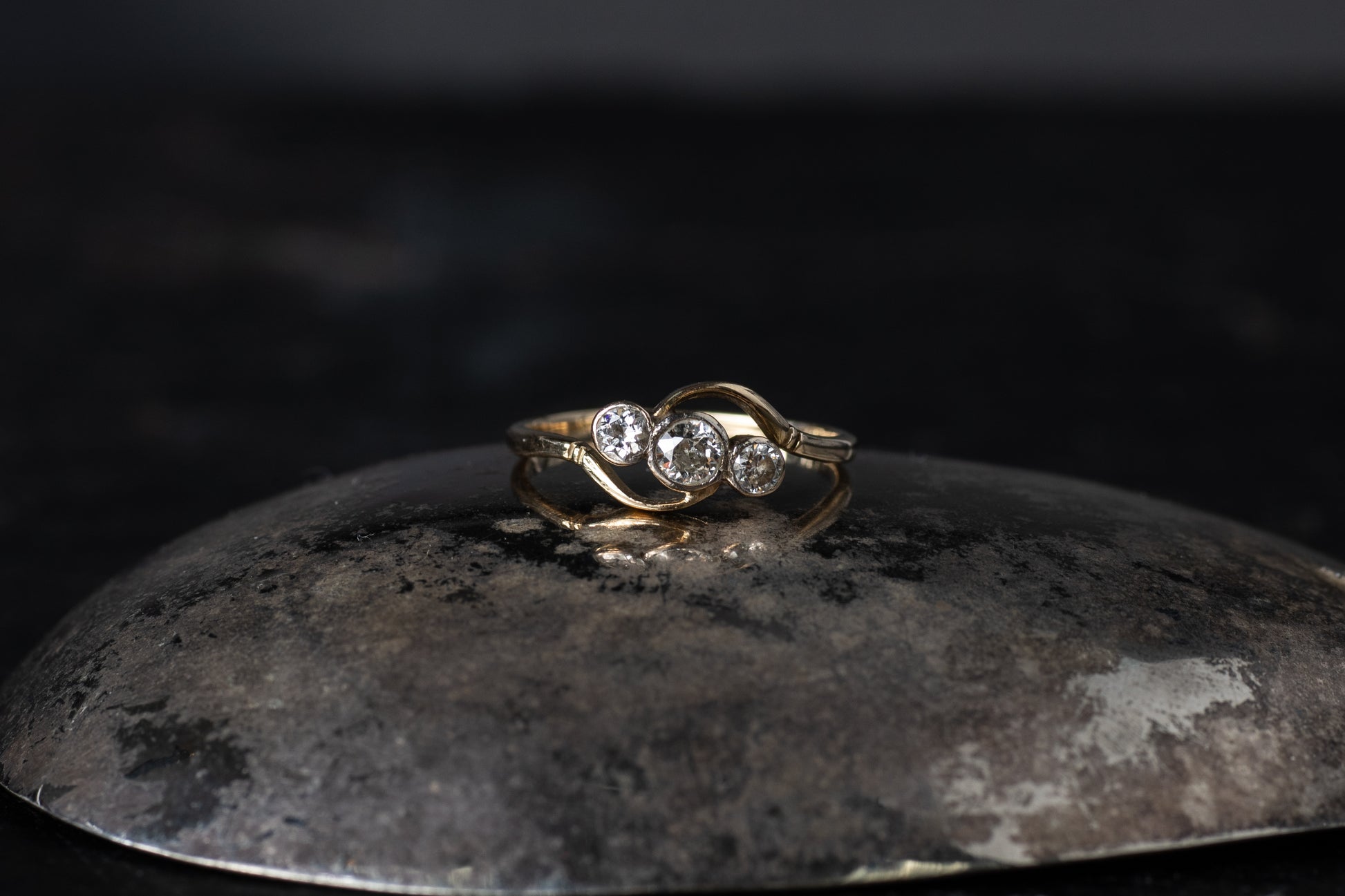 18ct yellow gold antique twist ring featuring three rub-over set diamonds on a dark reflective background.