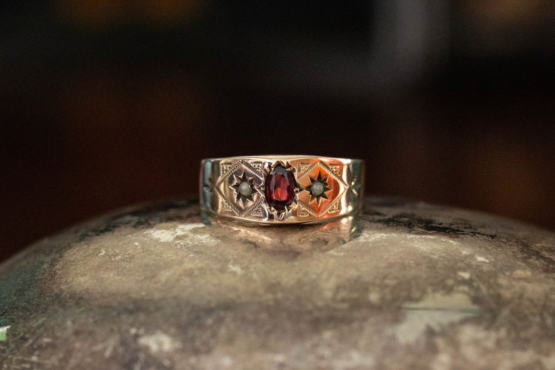 9ct yellow gold vintage band ring featuring a central oval garnet and star set seed pearls on a dark reflective surface.