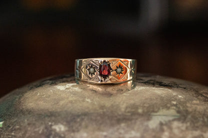 9ct yellow gold vintage band ring featuring a central oval garnet and star set seed pearls on a dark reflective surface.