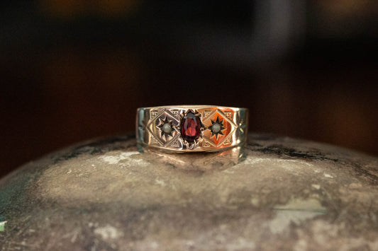 9ct yellow gold vintage band ring featuring a central oval garnet and star set seed pearls on a dark reflective surface.