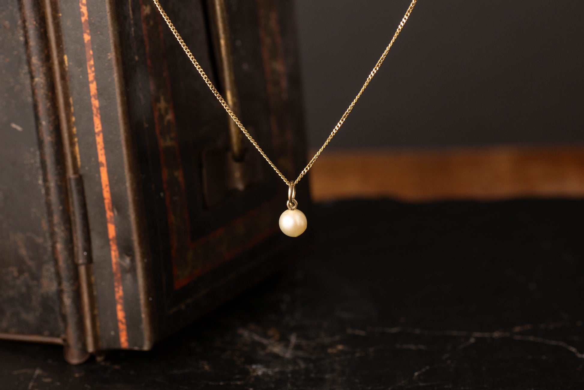 9ct yellow gold chain necklace featuring a single vintage white pearl pendant against a dark background.