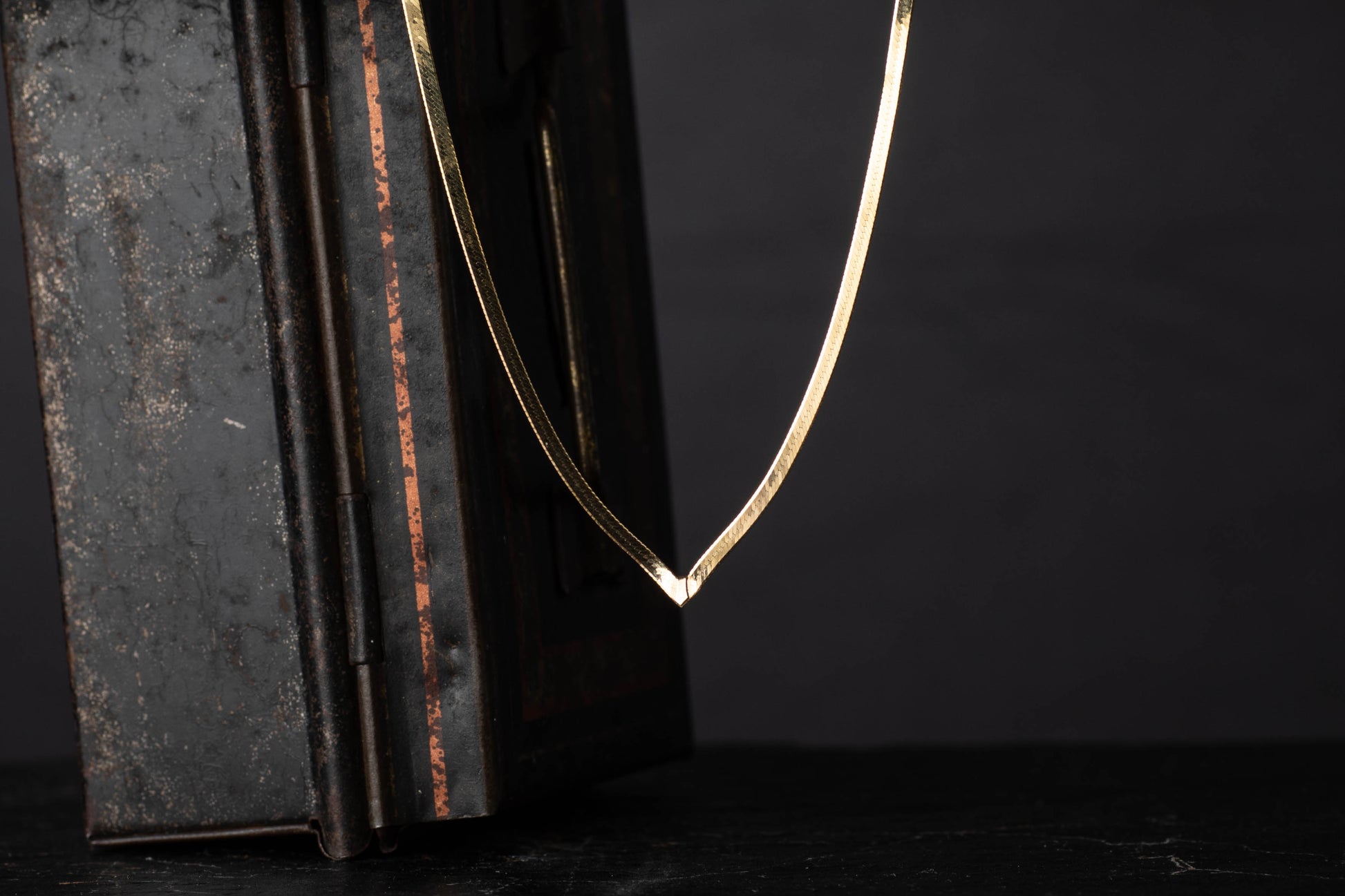9ct yellow gold vintage flat link necklace with V-shaped drop hanging against a dark background.