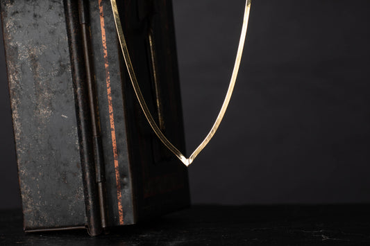 9ct yellow gold vintage flat link necklace with V-shaped drop hanging against a dark background.