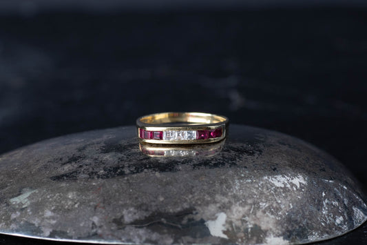 18ct yellow gold band ring featuring channel set baguette rubies and diamonds on a dark reflective surface.
