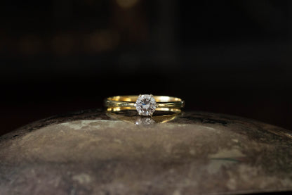 18ct yellow gold ring featuring a solitary brilliant cut diamond in a claw setting on a dark reflective background.