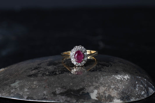 Antique cluster ring featuring an oval ruby surrounded by diamonds set in platinum on an 18ct yellow gold band.