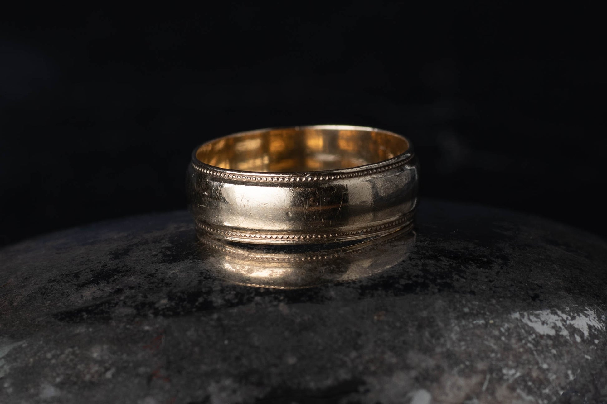 9ct yellow gold vintage wedding band ring with milgrain beaded edge detail on a dark reflective surface.