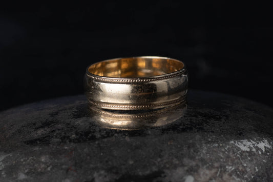 9ct yellow gold vintage wedding band ring with milgrain beaded edge detail on a dark reflective surface.