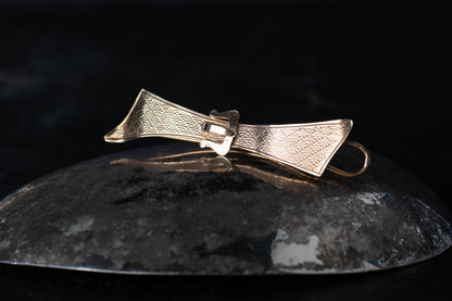 9ct yellow gold bow-shaped hair clip featuring a textured cross-hatch pattern and buckle detail on a dark surface.