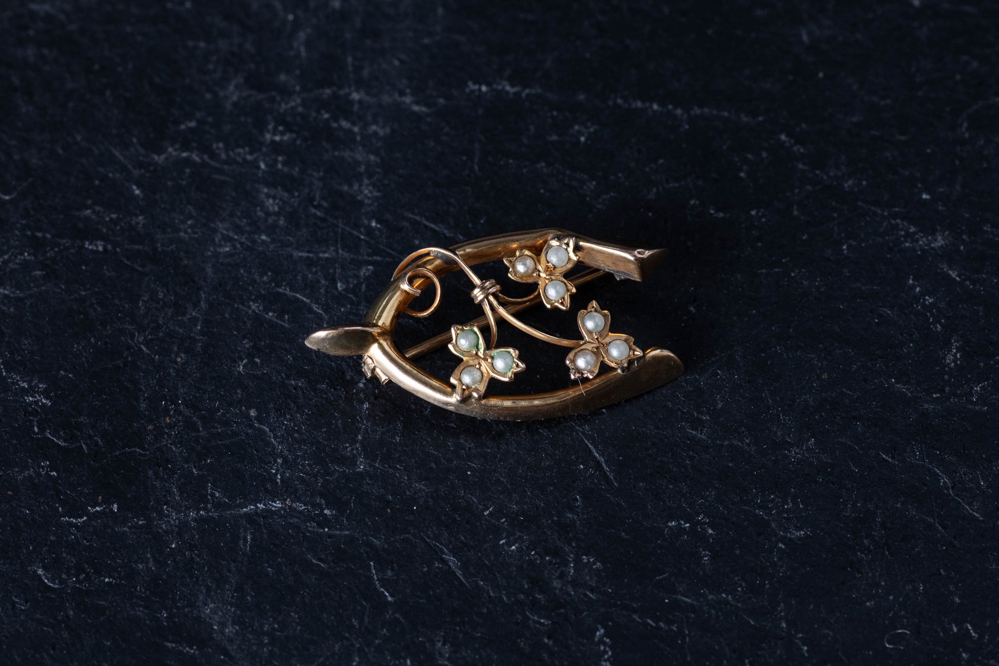9ct yellow gold antique wishbone brooch featuring seed pearl set shamrocks on a dark surface.