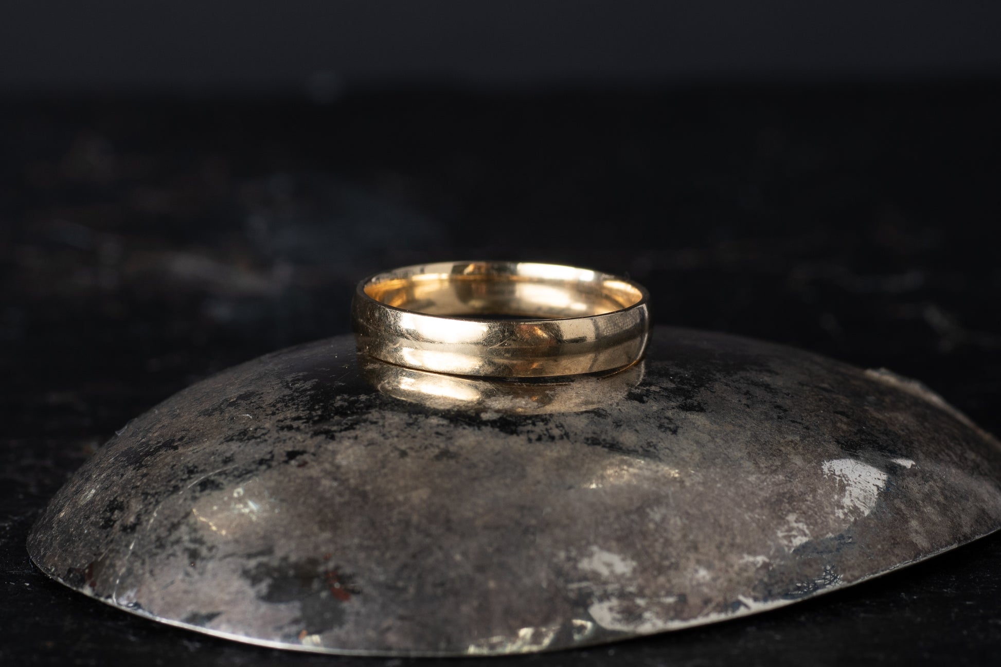 Plain 9ct yellow gold vintage mens wedding band ring resting on a dark reflective surface.