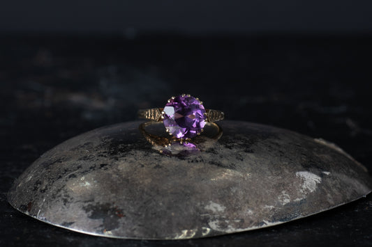 9ct yellow gold vintage ring featuring a round solitaire amethyst claw set with textured shoulders on a dark reflective surface.