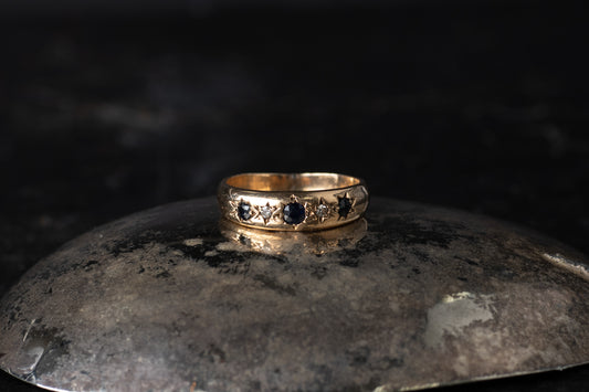 9ct yellow gold ring featuring five alternating star-set sapphires and diamonds on a dark reflective surface.