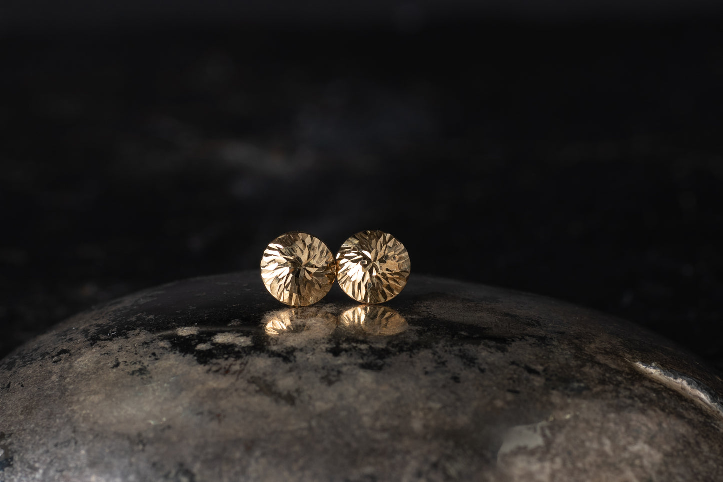 Pair of 9ct yellow gold dome stud earrings with a faceted textured surface resting on a dark reflective background.