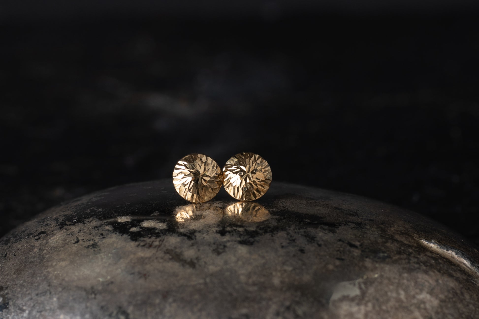 Pair of 9ct yellow gold dome stud earrings with a faceted textured surface resting on a dark reflective background.