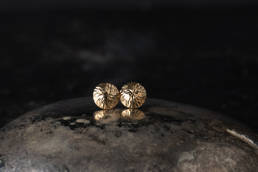 Pair of 9ct yellow gold dome stud earrings with a faceted textured surface resting on a dark reflective background.