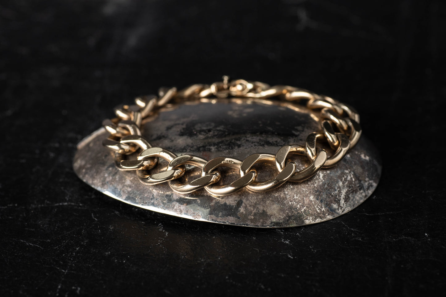 9ct yellow gold curb link bracelet featuring polished interlocking links resting on a dark reflective surface.