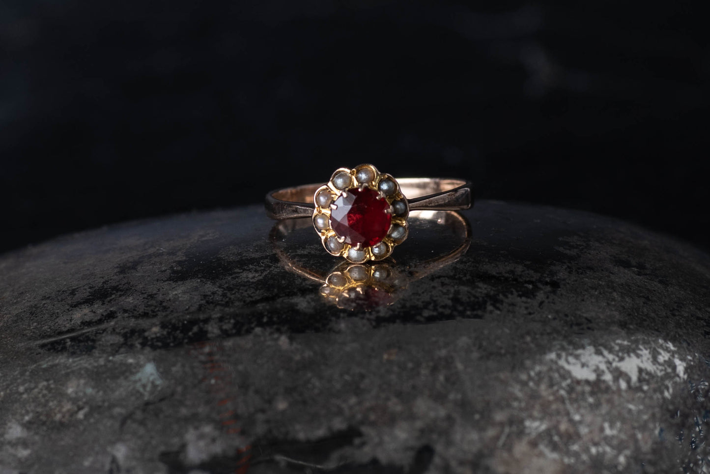 9ct yellow gold cluster ring featuring a central round paste ruby surrounded by a halo of seed pearls on a dark surface.9ct yellow gold cluster ring featuring a central round paste ruby surrounded by a halo of seed pearls on a dark surface.