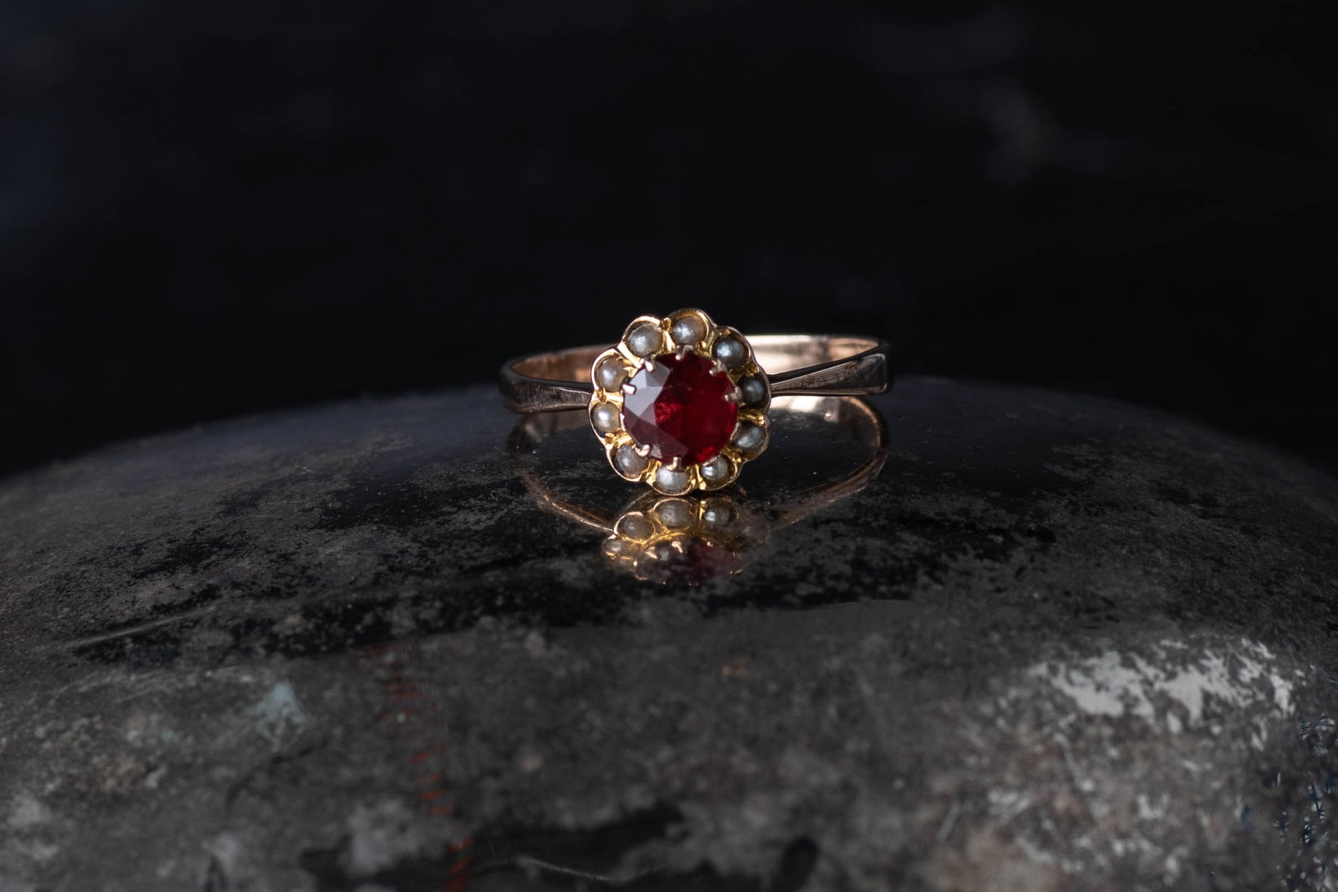 9ct yellow gold cluster ring featuring a central round paste ruby surrounded by a halo of seed pearls on a dark surface.9ct yellow gold cluster ring featuring a central round paste ruby surrounded by a halo of seed pearls on a dark surface.