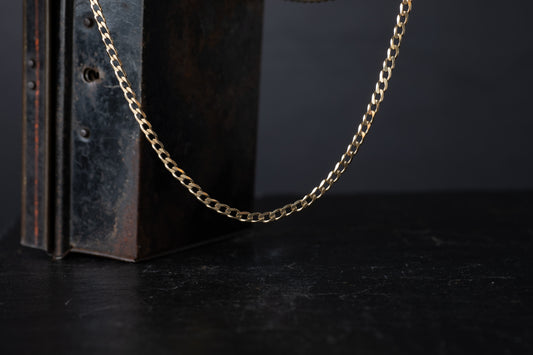 9ct yellow gold flat bevelled curb link chain necklace hanging against a dark vintage box background.