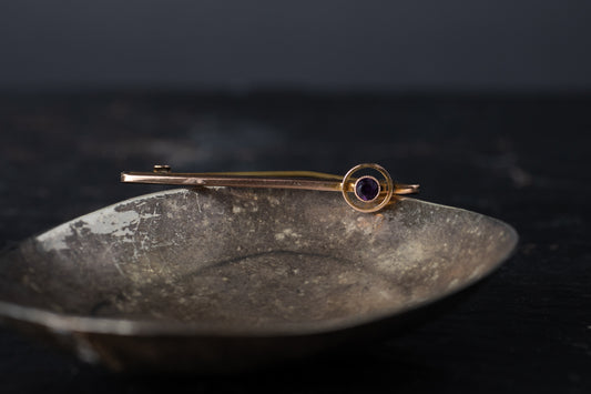 Vintage 9ct rose gold tie pin featuring a round solitaire amethyst set in a circular design on a dark metallic dish.