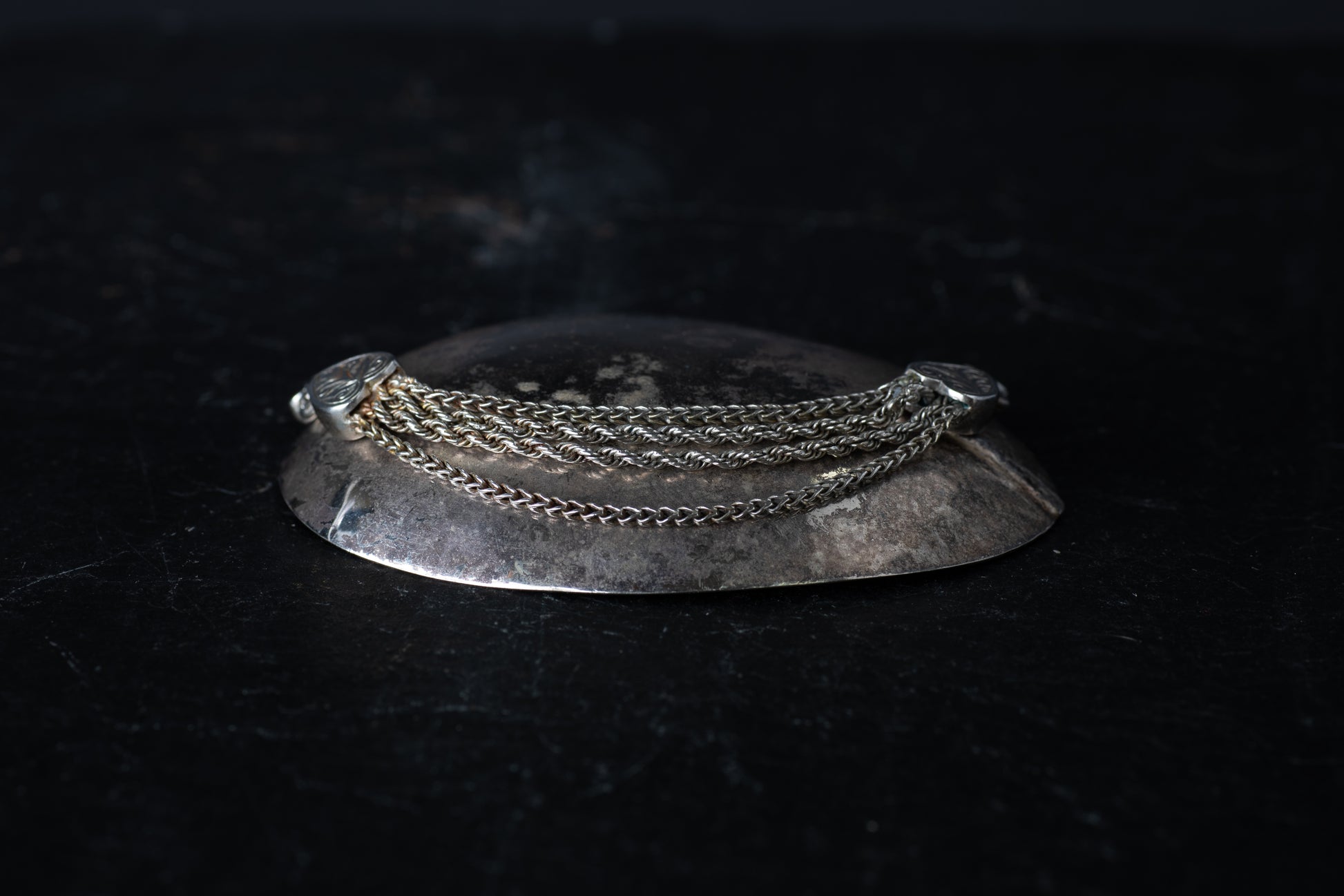Antique silver bracelet featuring multiple mixed link chains connected to heart-shaped terminals on a dark reflective surface.