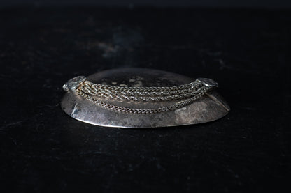 Antique silver bracelet featuring multiple mixed link chains connected to heart-shaped terminals on a dark reflective surface.