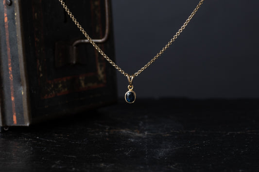 9ct yellow gold pendant featuring a rub over set oval blue sapphire hanging against a dark vintage box.