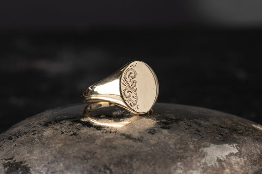 9ct yellow gold oval signet ring featuring a scroll engraved pattern on one half of the face.
