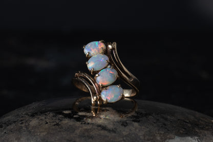 9ct yellow gold ring featuring four oval cabochon opals arranged in a diagonal twist setting on a dark surface.