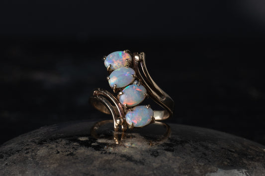 9ct yellow gold ring featuring four oval cabochon opals arranged in a diagonal twist setting on a dark surface.