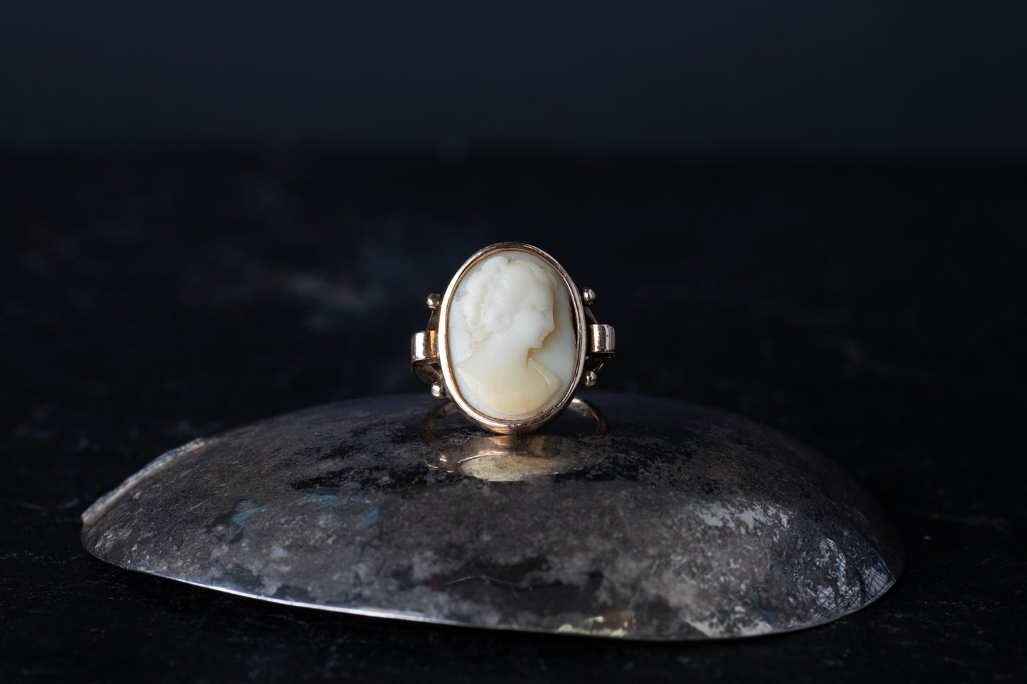 Antique 9ct rose gold ring featuring a rub over set oval Mother of Pearl cameo profile on a dark reflective surface.