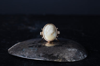Antique 9ct rose gold ring featuring a rub over set oval Mother of Pearl cameo profile on a dark reflective surface.